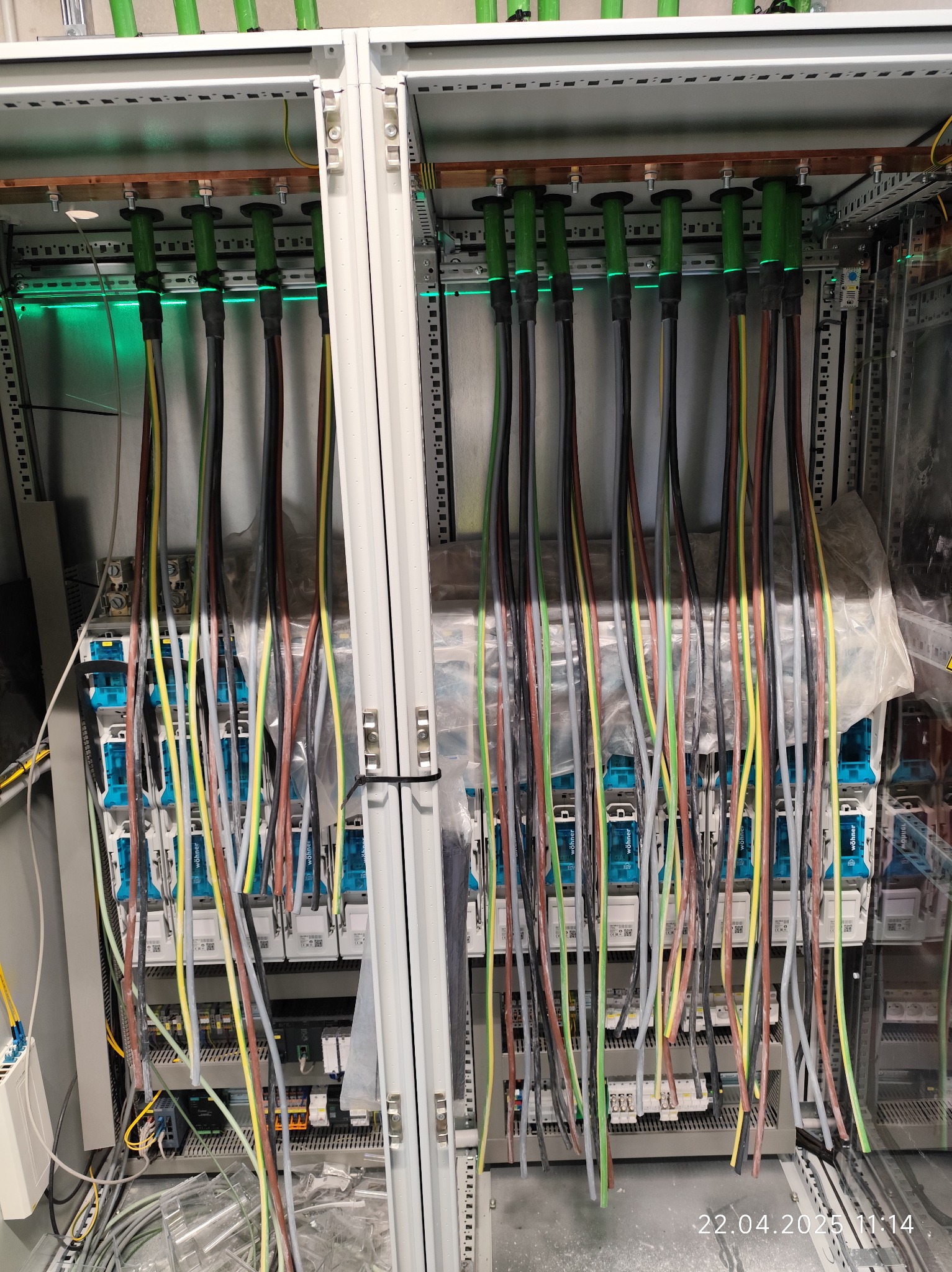 Rozdzielnica elektryczna z licznymi przewodami w różnych kolorach, podłączonymi do aparatury. Widoczne elementy montażowe i kable w peszlach. Oświetlenie LED wewnątrz szafy.