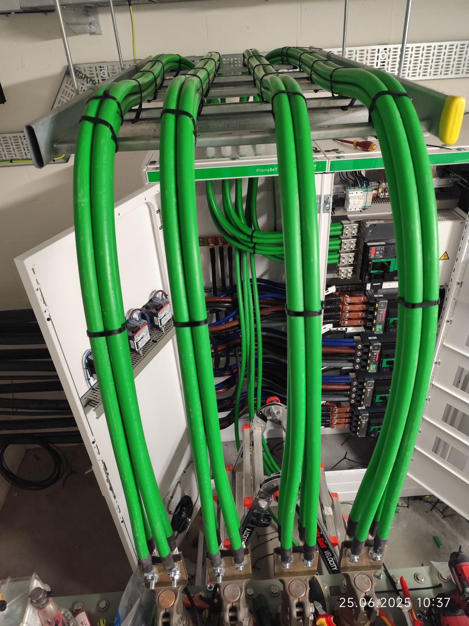 Zestaw zielonych kabli elektrycznych w osłonie, starannie ułożonych w szafie sterowniczej. Widoczne elementy montażowe i narzędzia, co sugeruje profesjonalny montaż.