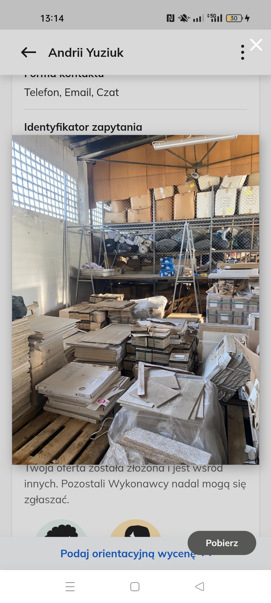 Stare płytki i gruz w magazynie, prawdopodobnie pozostałości po remoncie. Na półkach kartony i worki. Widok na wnętrze magazynu z metalową konstrukcją.