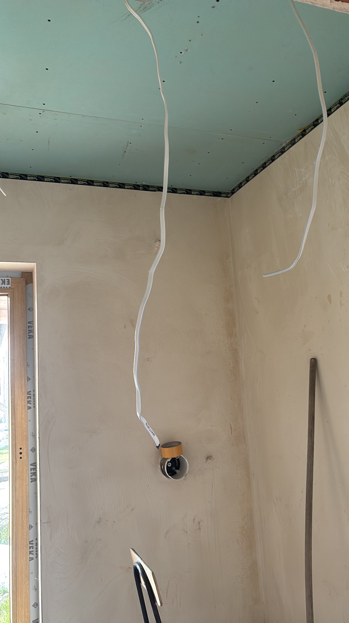 Ściana po szpachlowaniu z wystającymi przewodami elektrycznymi i zamontowaną puszką. Sufit z płyt kartonowo-gipsowych. Widoczne narzędzia.