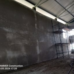 Kuba kępski - Ściana po szpachlowaniu w hali, widoczne ślady po pracy i rusztowanie. Surowy stan, przygotowanie do dalszych prac wykończeniowych.