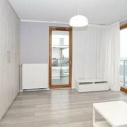 Kuba kępski - Jasne, przestronne wnętrze po remoncie: parkiet, białe ściany, okno balkonowe z drewnianą ramą, minimalistyczne meble i wisząca lampa. Widok na miasto w tle.