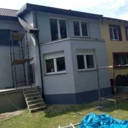 Kuba kępski - Szary dom po malowaniu elewacji z rusztowaniem, widok z ogrodu. Dolna część elewacji w ciemniejszym odcieniu szarości. Okna z białymi ramami.