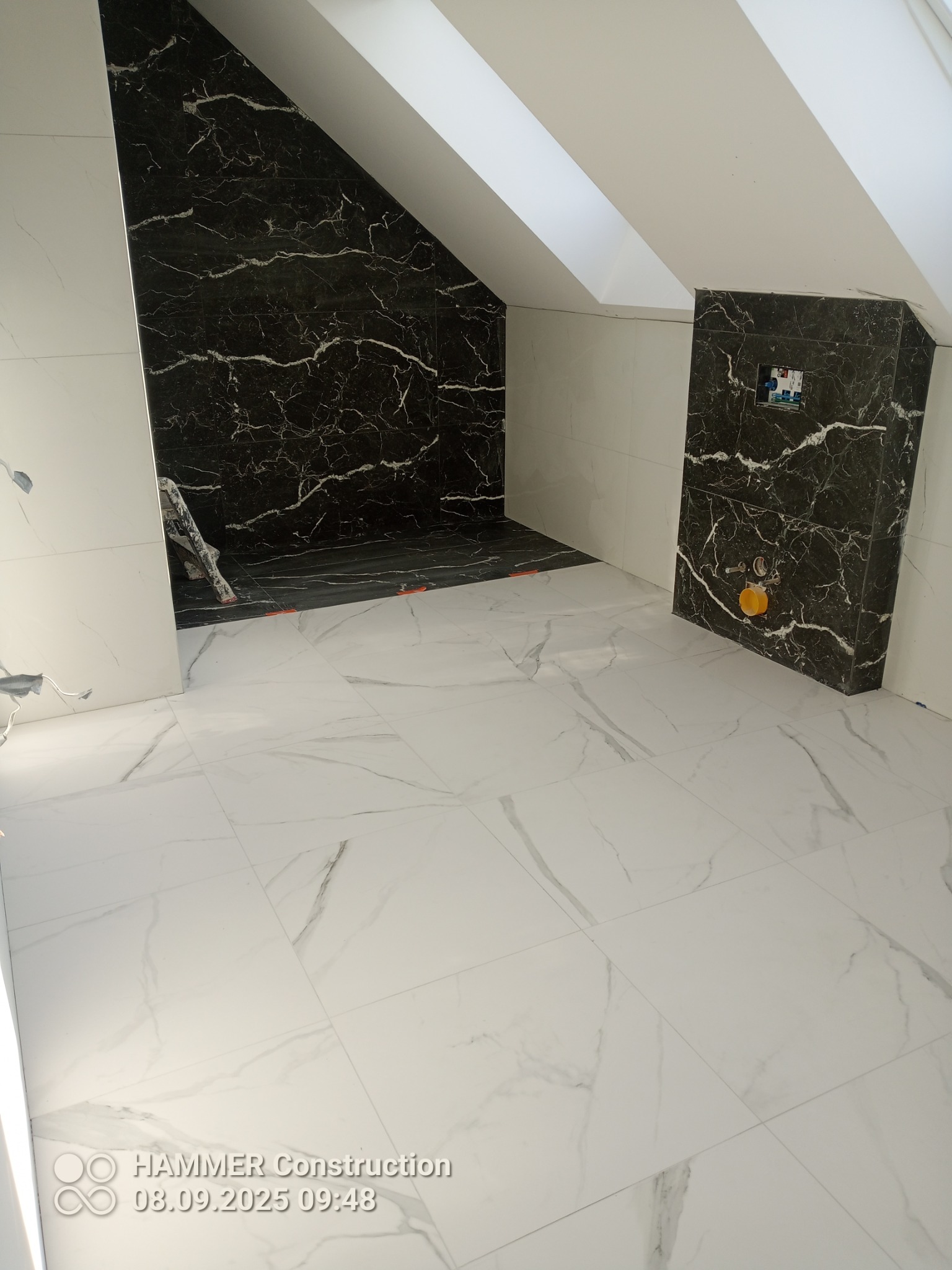 Wykończona łazienka na poddaszu w Słupsku z czarno-białymi płytkami imitującymi marmur na podłodze i ścianach kabiny prysznicowej.