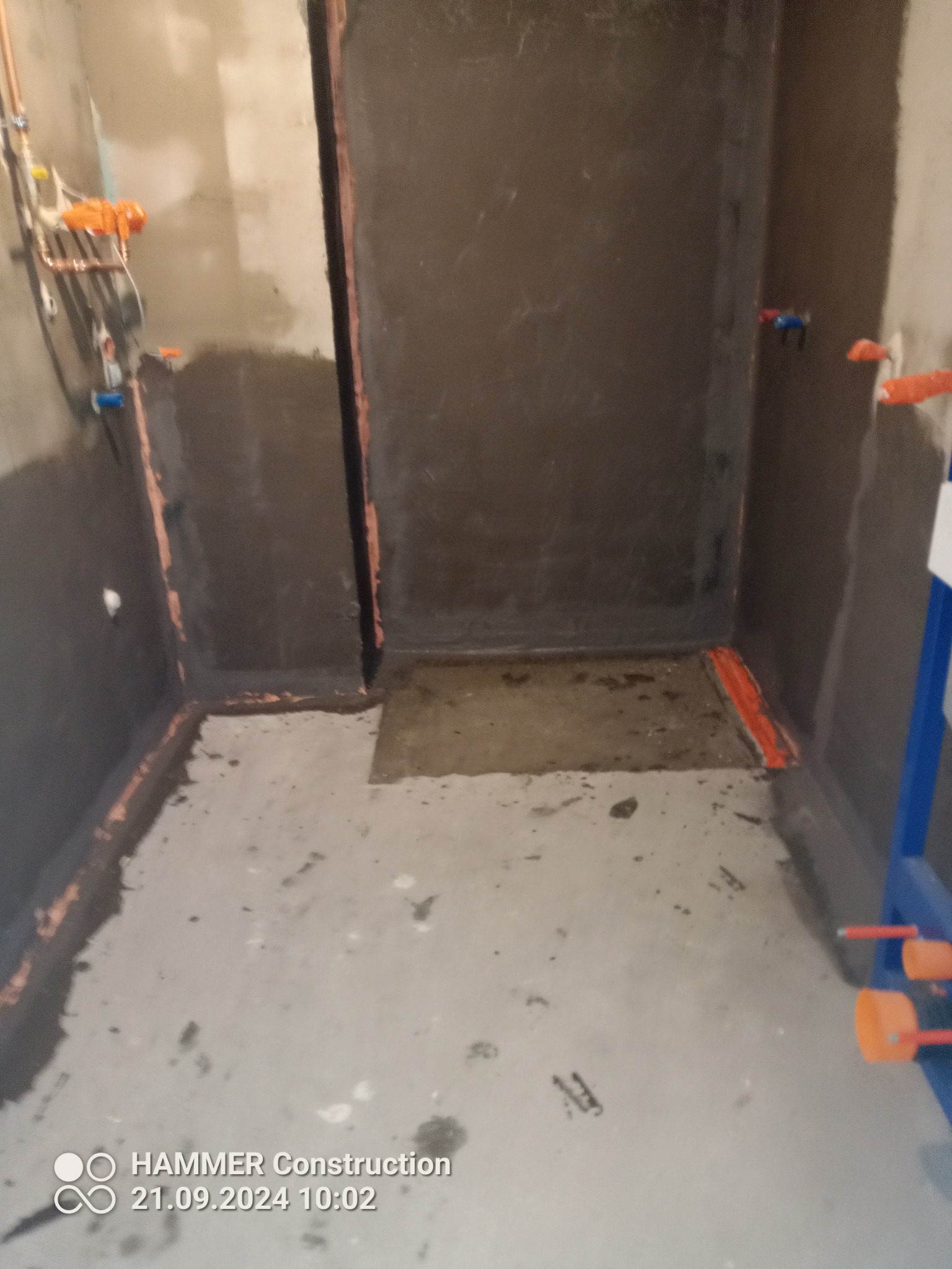 Hydroizolacja w trakcie prac w łazience: zabezpieczone ściany i podłoga, widoczne rury instalacji wodnej. Etap przygotowania do dalszych prac wykończeniowych.
