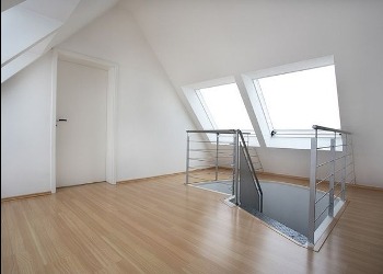 Jasne poddasze po remoncie: drewniana podłoga, białe ściany, schody z metalową barierką i dwa okna dachowe w skosie. Minimalistyczny design.