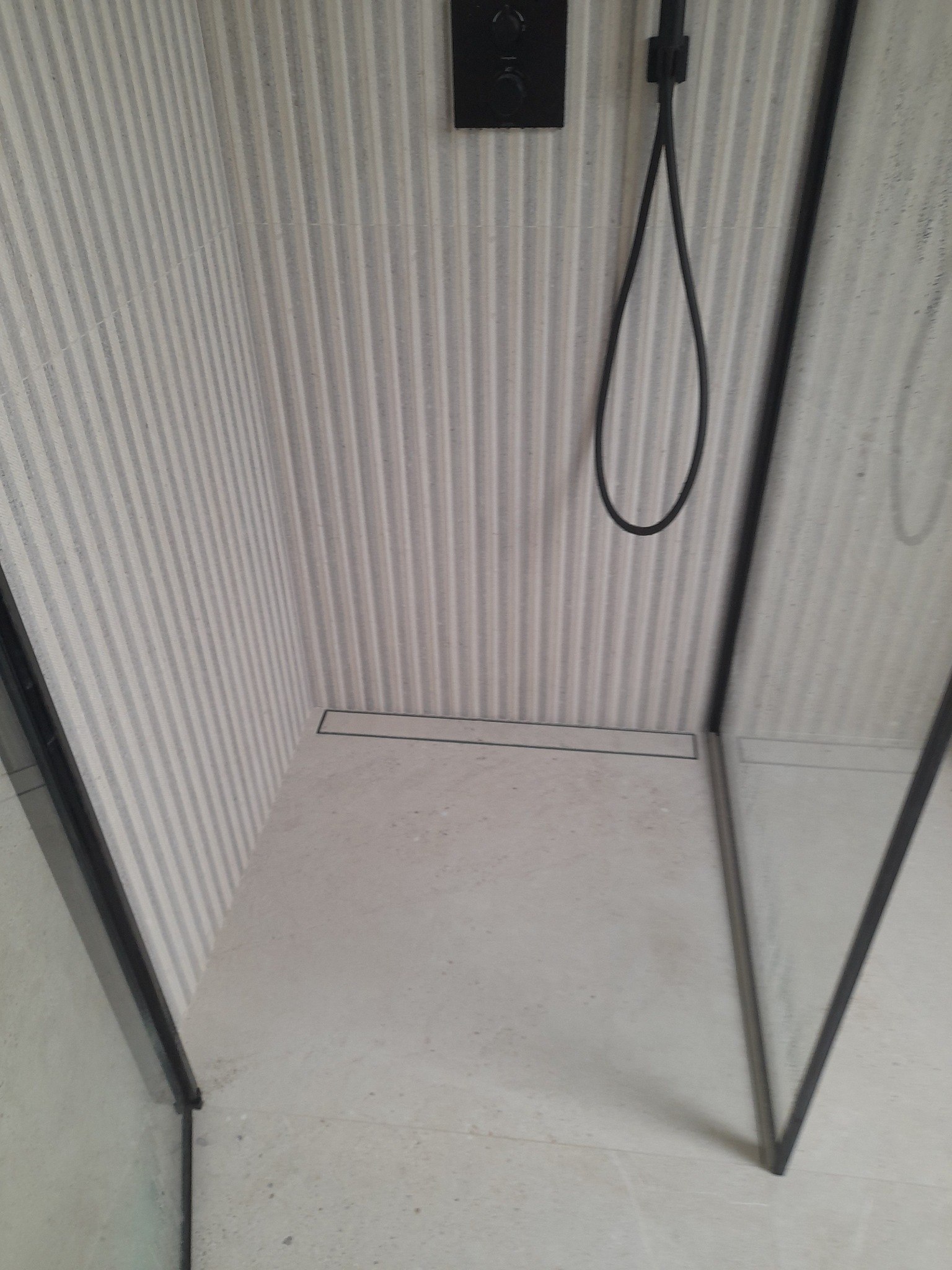 Nowoczesna kabina prysznicowa walk-in z odpływem liniowym, wykończona płytkami w pionowe prążki i czarną armaturą, prezentująca minimalistyczny design łazienki.