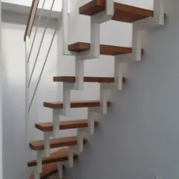 Nowoczesne schody drewniane z białymi metalowymi wspornikami i minimalistyczną balustradą, z widoczną ceglaną ścianą w tle.