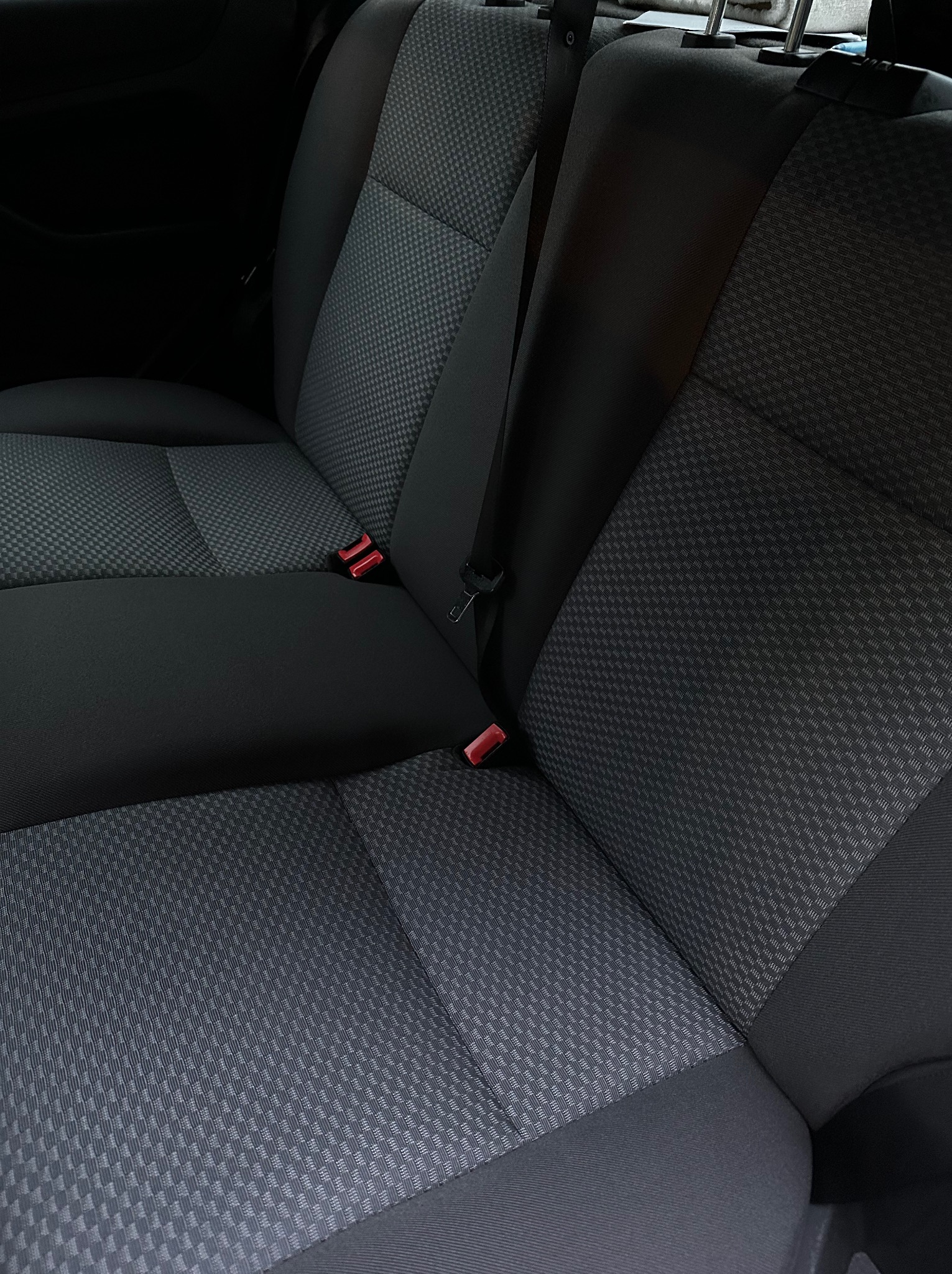 Wnętrze samochodu: tylna kanapa z szarą tapicerką w drobną kratkę, widoczne pasy bezpieczeństwa. Czysta, zadbana powierzchnia po usłudze.