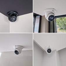 Cztery kamery kopułkowe monitoringu, zamontowane w rogach sufitów o różnej kolorystyce, ukazane z bliska, z widocznymi obiektywami i fragmentami otoczenia.