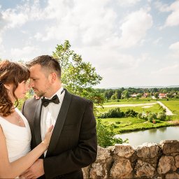 Studio4U - Para młoda w objęciach na tle malowniczego krajobrazu z jeziorem i zielenią. Pan młody w smokingu, panna młoda w białej sukni. Romantyczna atmosfera.