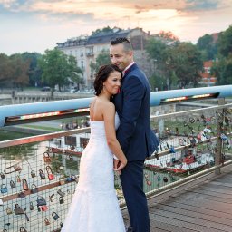 Studio4U - Para młoda na moście zakochanych, wieczorne światło, widok na miasto w tle. Most ozdobiony kłódkami symbolizującymi miłość.