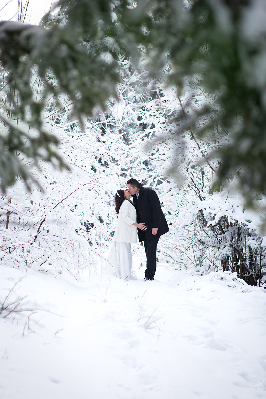 Pocałunek w zimowej scenerii: Para młoda w lesie, otulona śniegiem, w romantycznym ujęciu z bliska, z delikatnym rozmyciem gałęzi w górnej części kadru.