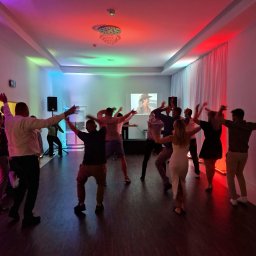 NEXA ENERGY Leszek Korycki - Roztańczona grupa osób w sali z kolorowym oświetleniem, balony i projektor w tle. Dynamiczna scena z imprezy integracyjnej.