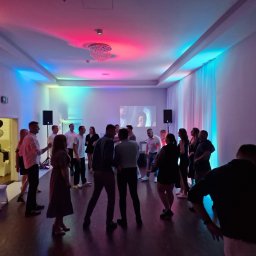 NEXA ENERGY Leszek Korycki - Impreza firmowa w sali z oświetleniem LED: tańczący ludzie, balony, projektor wyświetlający obraz. Kolorowe światła na suficie i ścianach tworzą radosną atmosferę.