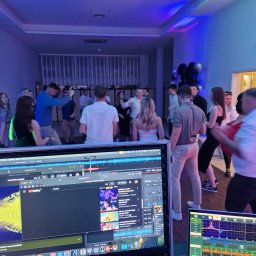 NEXA ENERGY Leszek Korycki - Impreza firmowa w niebieskim oświetleniu, z widocznymi monitorami DJ-a i tańczącymi osobami w tle. Dynamiczna atmosfera zabawy.