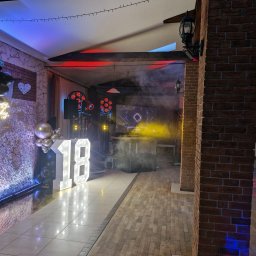 NEXA ENERGY DJ event Leszek Korycki - Udekorowana sala eventowa z podświetlanym napisem '18', czarnymi balonami i neonowym 'Happy Birthday'. Widoczny sprzęt DJ-ski z ruchomymi głowami, dymem i dynamicznym oświetleniem w barwach...