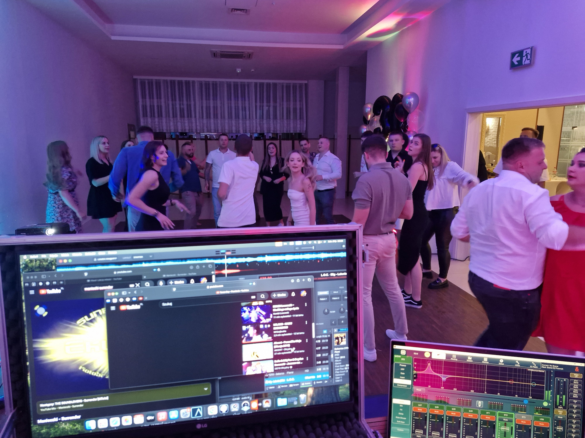 Parkiet taneczny wypełniony bawiącymi się ludźmi, oświetlony kolorowymi światłami. W tle widoczne ekrany z oprogramowaniem do miksowania muzyki, sugerujące oprawę DJ-ską.