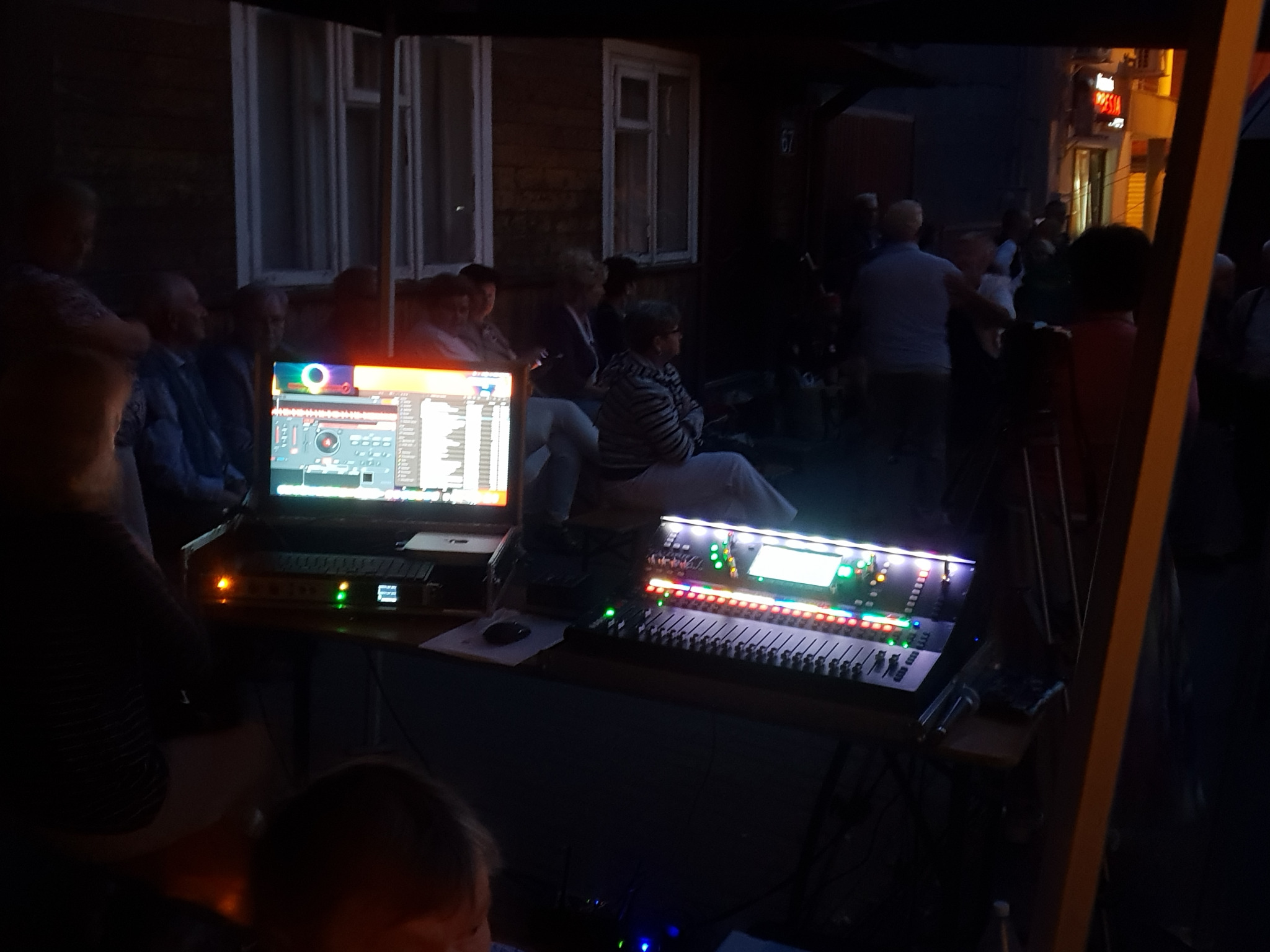 Konsoleta mikserska i monitor z oprogramowaniem DJ-skim podczas imprezy plenerowej w Garwolinie. W tle widoczni słuchacze i budynek.