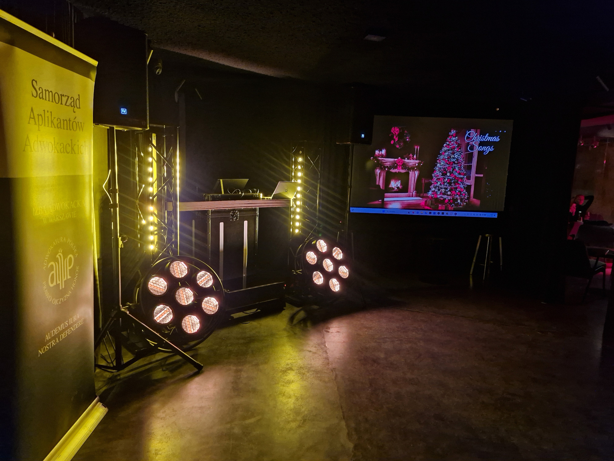 Scena z nagłośnieniem i oświetleniem, baner reklamowy Samorządu Aplikantów Adwokackich, ekran z motywem świątecznym. Przygotowania do wydarzenia.