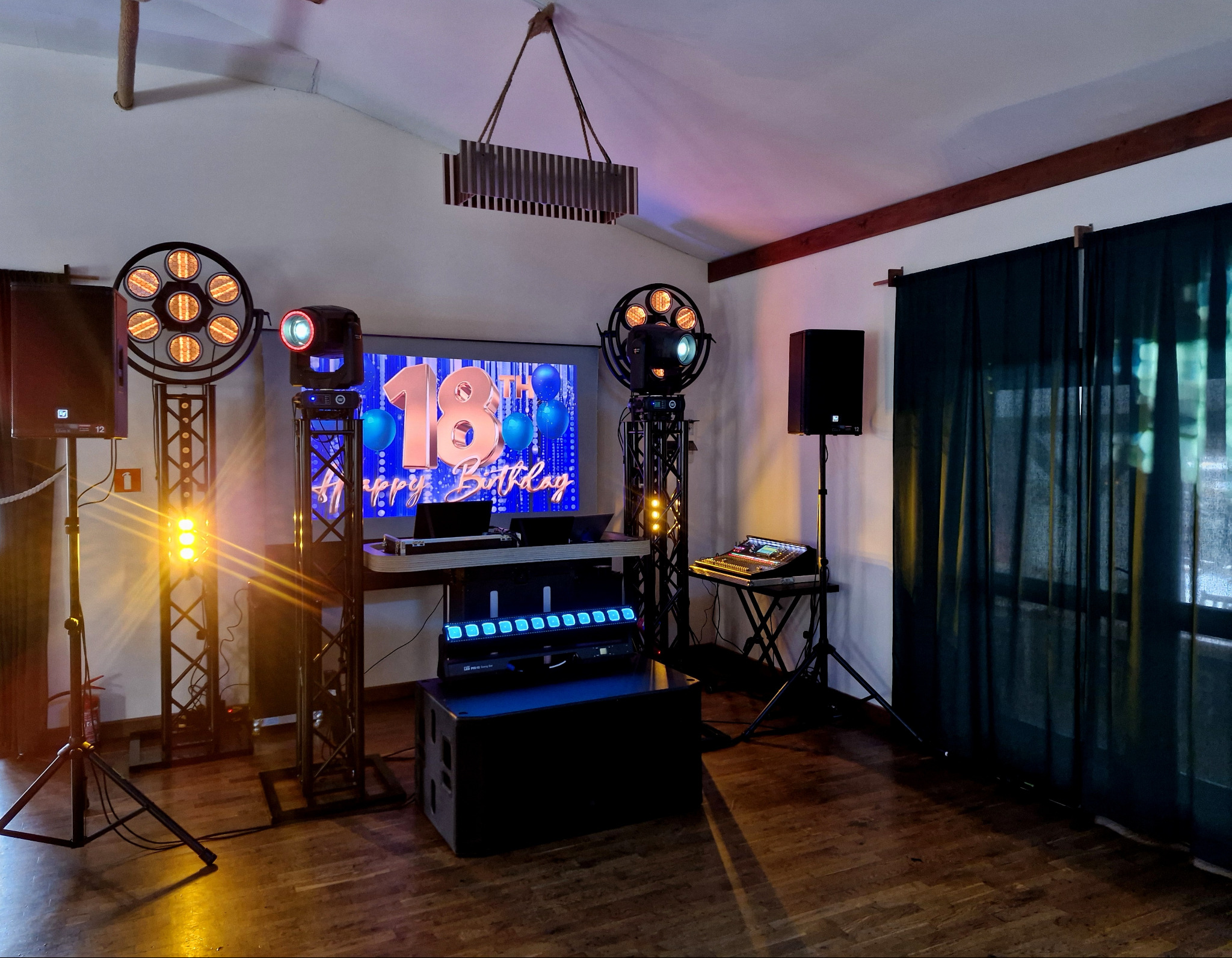 Sprzęt nagłośnieniowy i oświetleniowy na sali z ekranem wyświetlającym napis 'Happy Birthday 18th'.