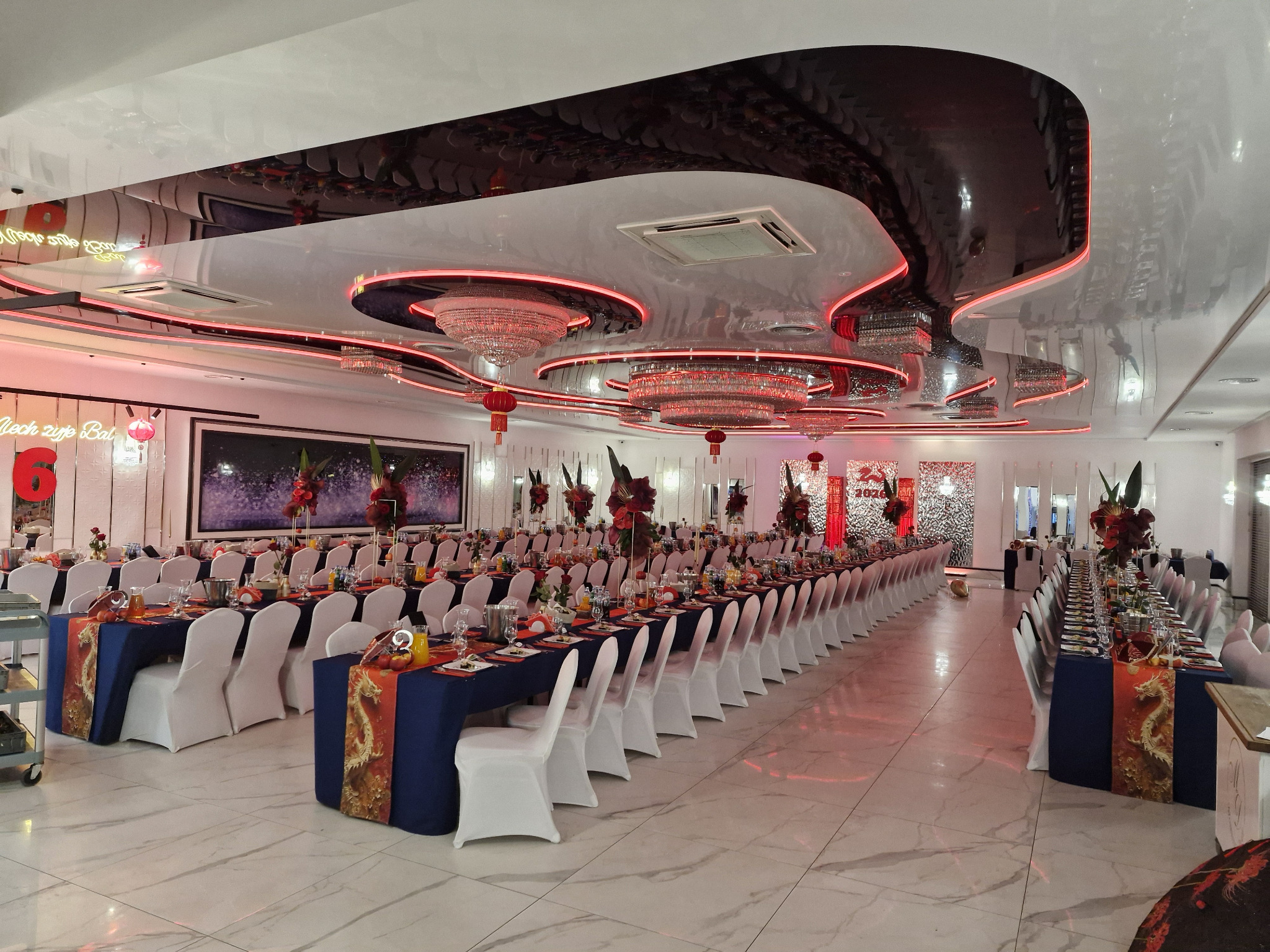 Uroczysta sala bankietowa z długimi stołami, nakryta do przyjęcia, z dekoracjami kwiatowymi i eleganckim oświetleniem, gotowa na imprezę.