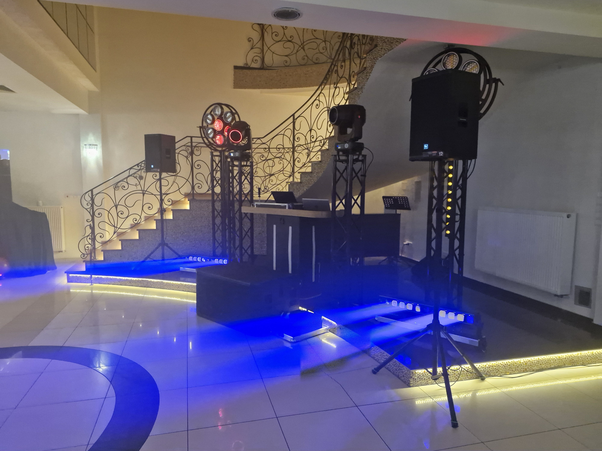 Scena z nagłośnieniem i oświetleniem w sali balowej z dekoracyjnymi schodami. Niebieskie światła LED na podeście i podświetlone schody tworzą klimat imprezy.