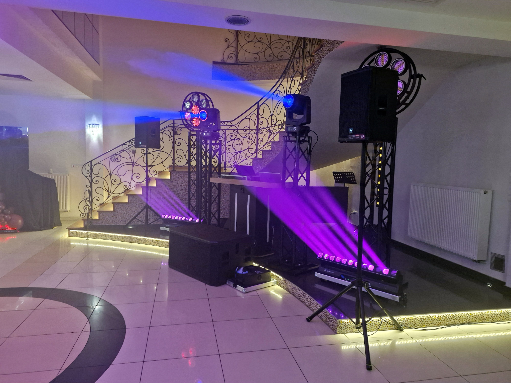 Profesjonalne nagłośnienie i oświetlenie sceniczne z reflektorami i kolumnami głośnikowymi, ustawione w eleganckim wnętrzu z dekoracyjnymi schodami.