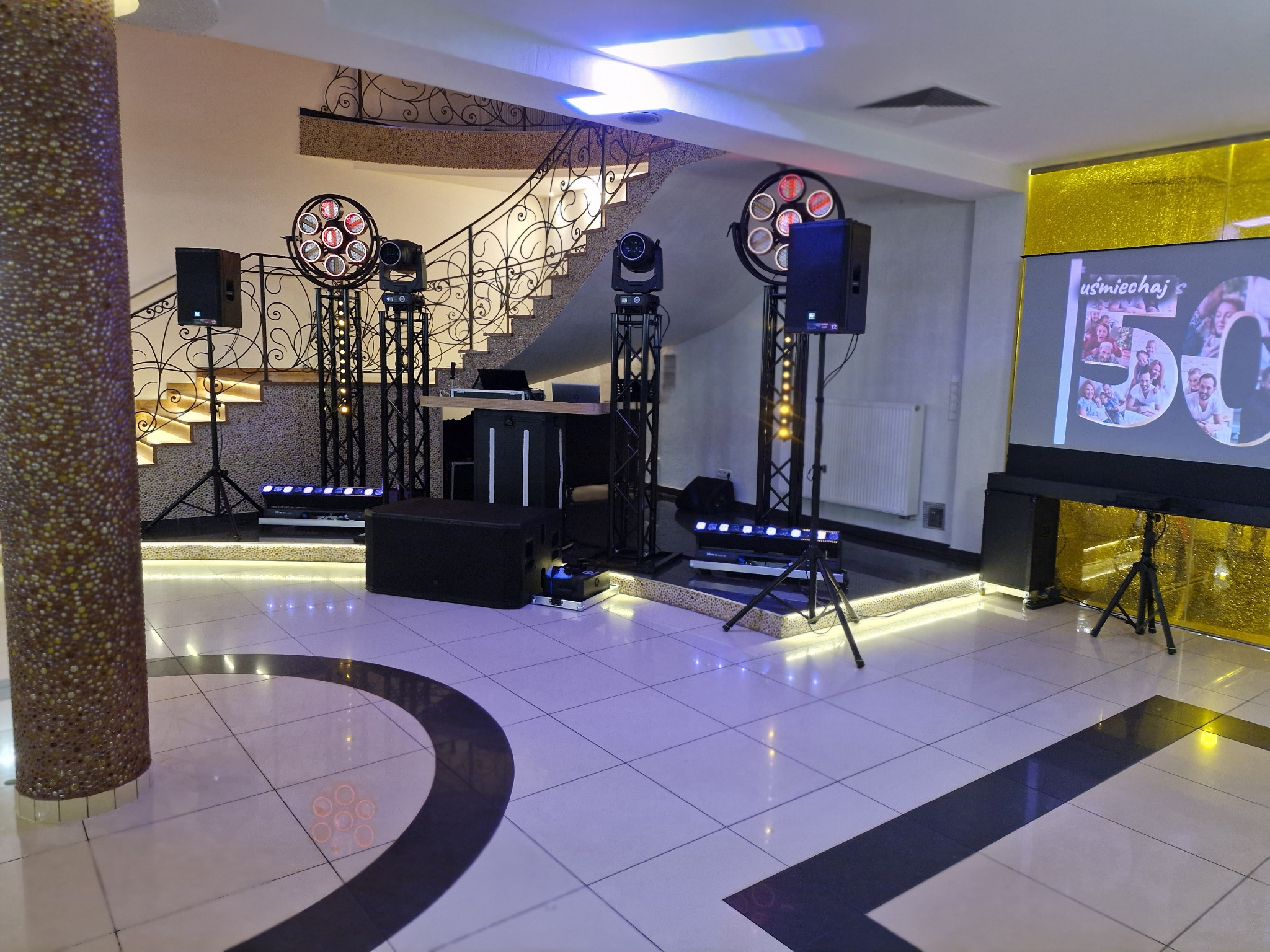Sala bankietowa z profesjonalnym nagłośnieniem i oświetleniem przygotowana na imprezę. Na ekranie wyświetlane zdjęcia z uroczystości.