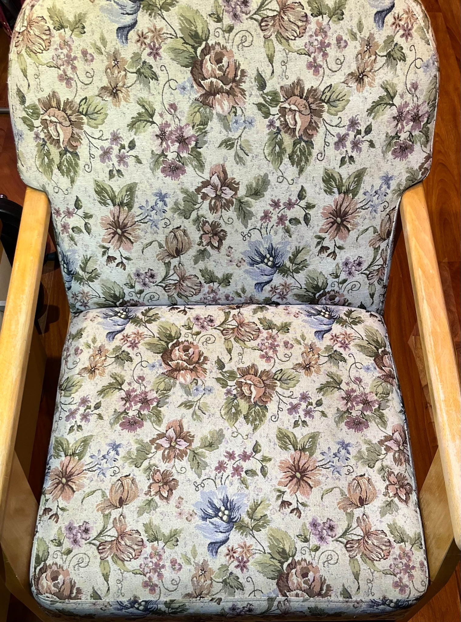 Welurowy fotel z drewnianymi podłokietnikami, obity tkaniną w kwiaty w odcieniach beżu, brązu i fioletu. Widok z góry na siedzisko i oparcie.