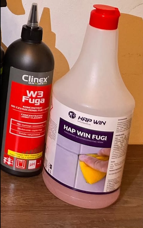 Dwa środki do czyszczenia fug: czarny Clintex W3 Fuga i biały Hap Win Fugi z aplikatorem, oba w plastikowych butelkach, na tle ściany i drewnianej półki.