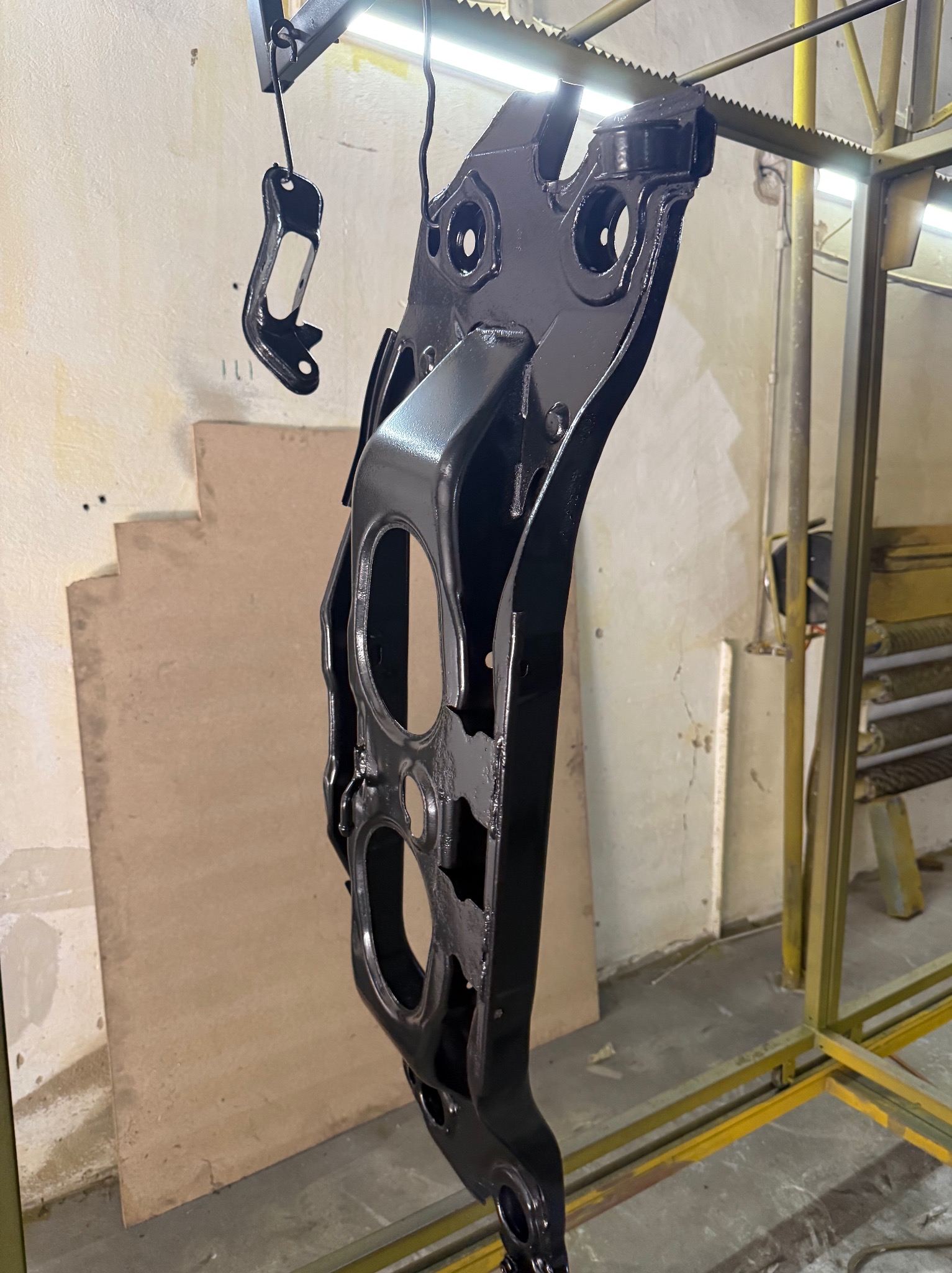 Część samochodowa po malowaniu proszkowym na czarno, zawieszona na haku w warsztacie. Widoczne ślady po procesie malowania.