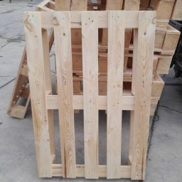 Palety Fitosanitarne I SPRZEDAŻ TARCICY LESZEK MICHALIK - Jasna, drewniana paleta na szarym tle, z widocznymi słojami drewna i konstrukcją. W tle stos palet, tworzący wzór powtarzalnych elementów.