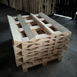 Palety Fitosanitarne I SPRZEDAŻ TARCICY LESZEK MICHALIK - Stos jasnych, drewnianych palet w magazynie, ułożonych jeden na drugim. W tle widoczne inne palety i ciemne ściany magazynu. Surowe drewno, widoczne słoje.