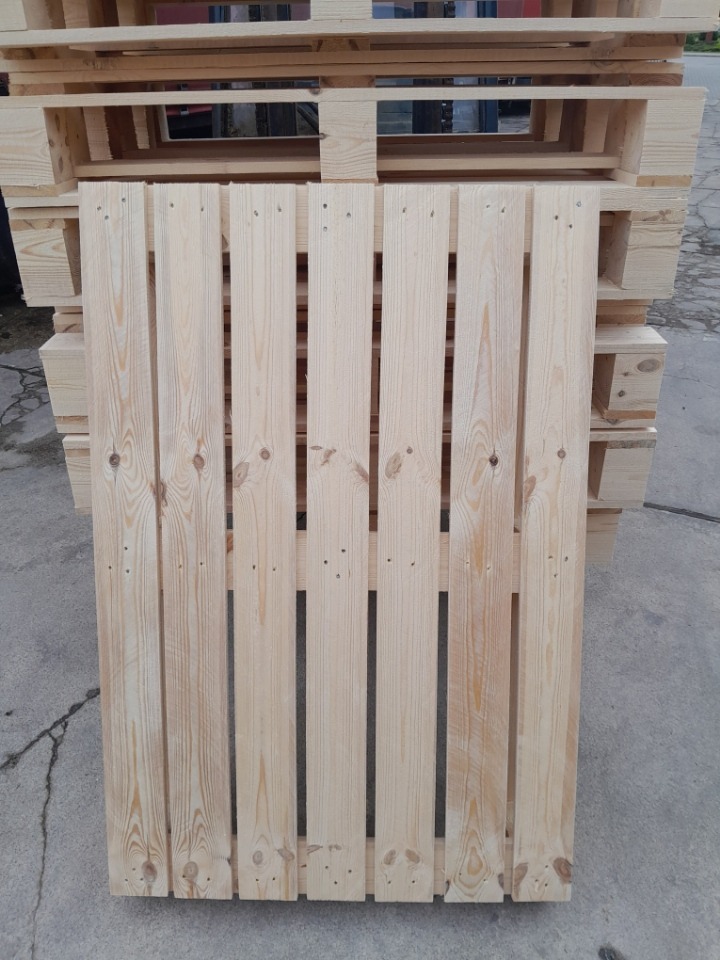 Jasna, drewniana paleta z widocznym rysunkiem słojów, ułożona na stosie innych palet. Widoczne gwoździe i naturalna struktura drewna.