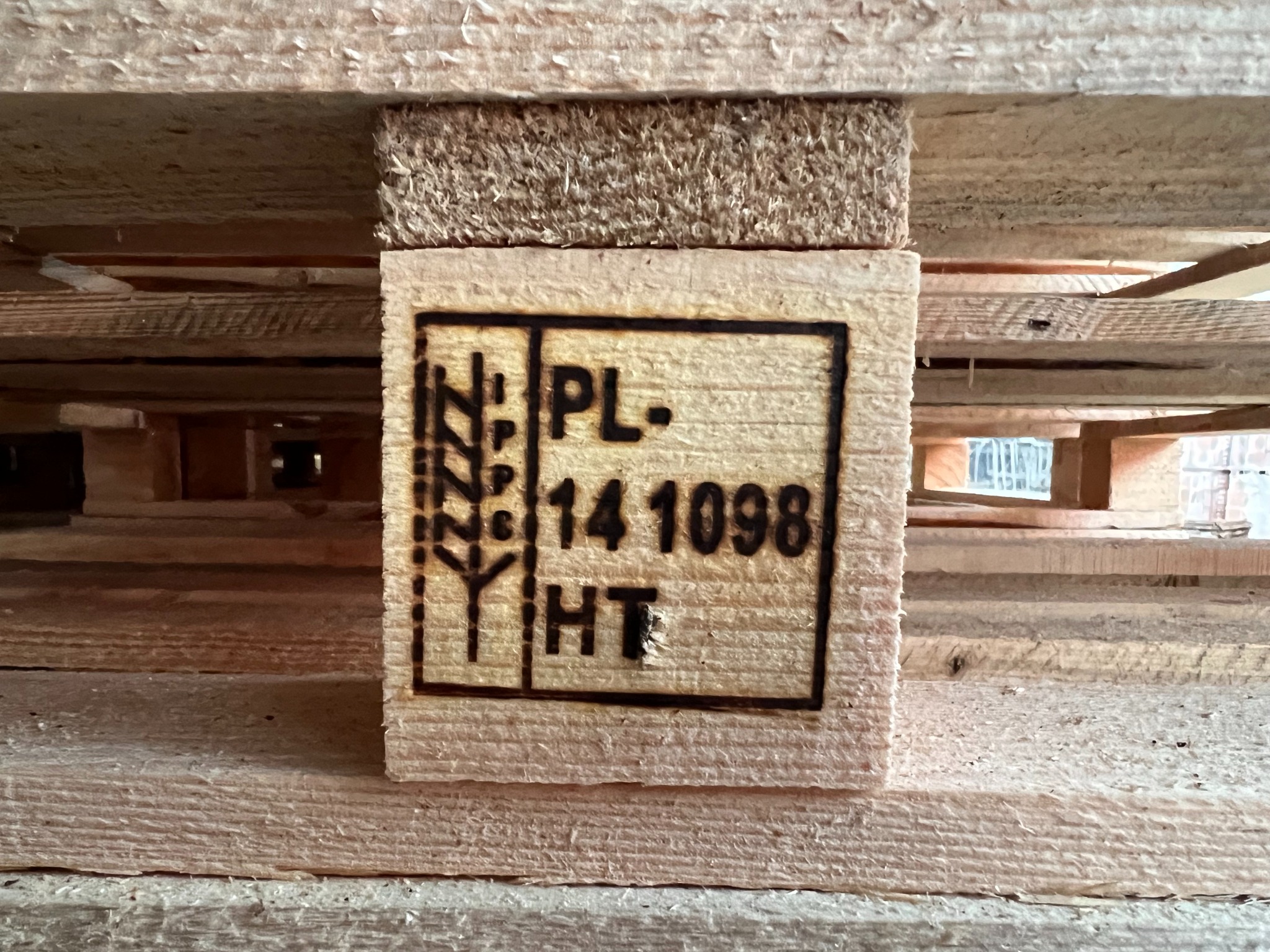 Fragment drewnianej palety z wypalonym oznaczeniem PL-14 1098 HT, widoczne elementy konstrukcyjne palety z surowego drewna.