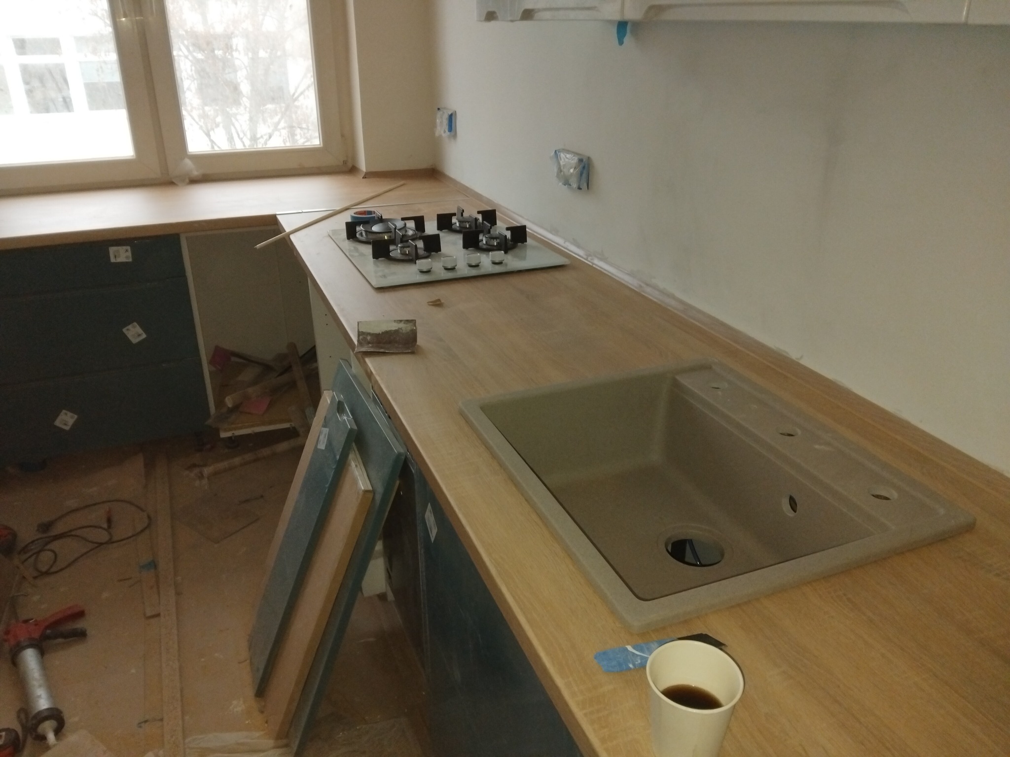 Montaż blatu kuchennego z płytą grzewczą i zlewem. Widoczne narzędzia i niedokończone szafki. Ujęcie z góry, naturalne światło.