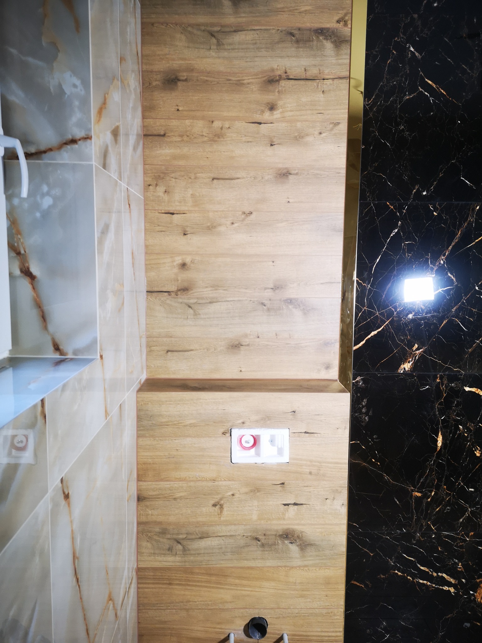 Wykończenie łazienki: połączenie płytek imitujących drewno, marmuru i onyksu z elementami złota. Widoczny fragment toalety podtynkowej.