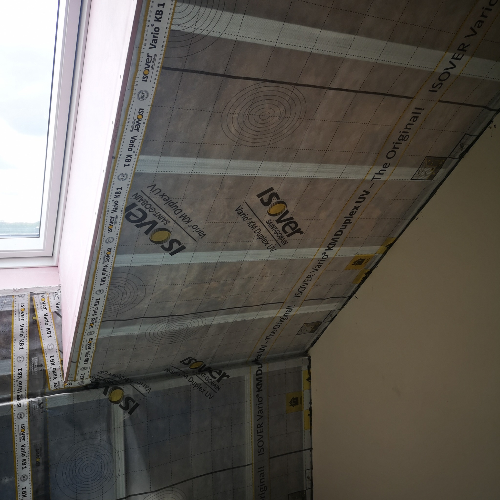 Izolacja poddasza z folią paroizolacyjną Isover Vario KM Duplex UV, widoczne łączenia i okno dachowe. Prace wykończeniowe na poddaszu.