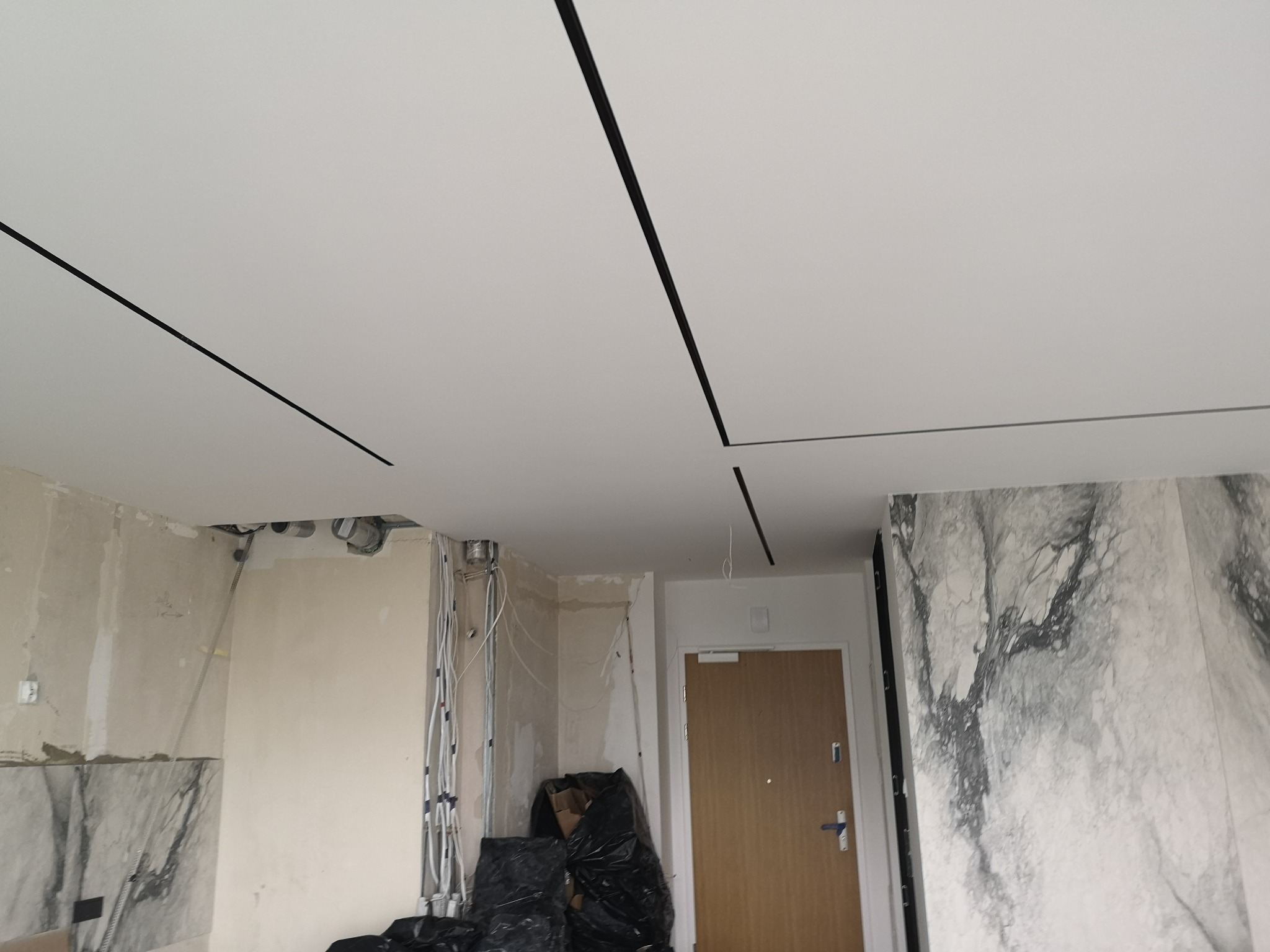 Biały sufit z czarnymi listwami dekoracyjnymi w trakcie wykańczania wnętrza. Widoczne ściany w stanie surowym i instalacje elektryczne.