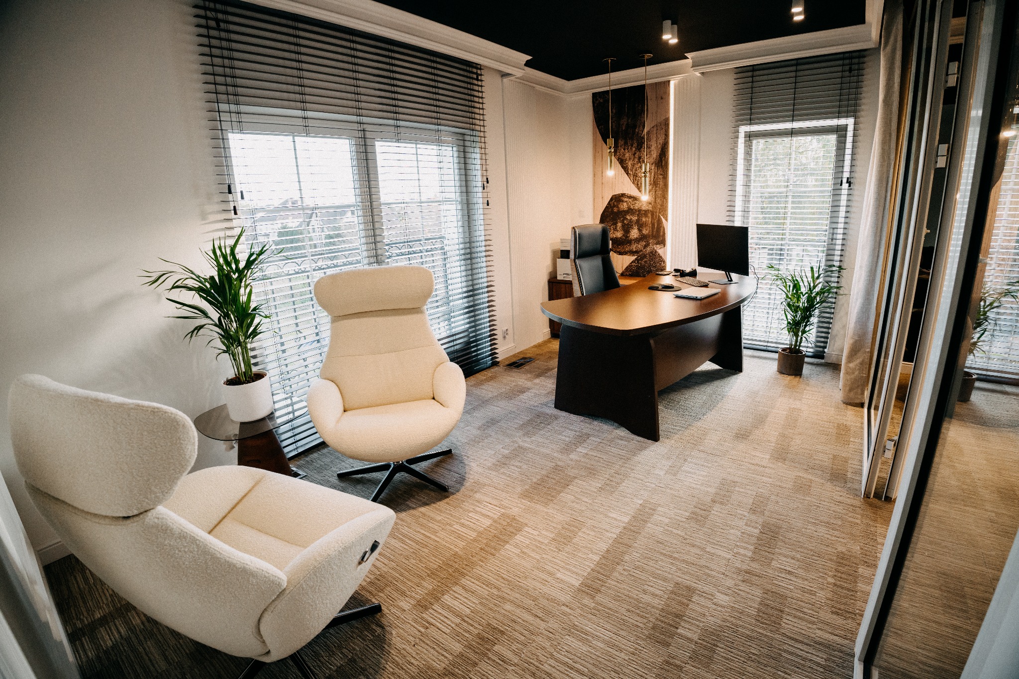 Eleganckie biuro z drewnianym biurkiem, ergonomicznymi fotelami i roślinami doniczkowymi. Stonowana kolorystyka, żaluzje w oknach, nowoczesne oświetlenie.