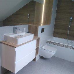 WW-REM - Nowoczesna łazienka na poddaszu z umywalką nablatową, białymi szafkami, toaletą podwieszaną i wanną z mozaiką. Uwagę zwraca oświetlenie LED za lustrem.