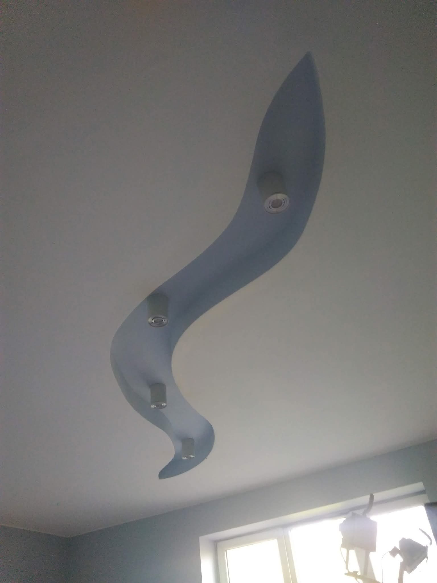 Falista, podwieszana konstrukcja sufitowa z oświetleniem punktowym, pomalowana na niebiesko, widoczna z dołu. Nowoczesny design wnętrza.