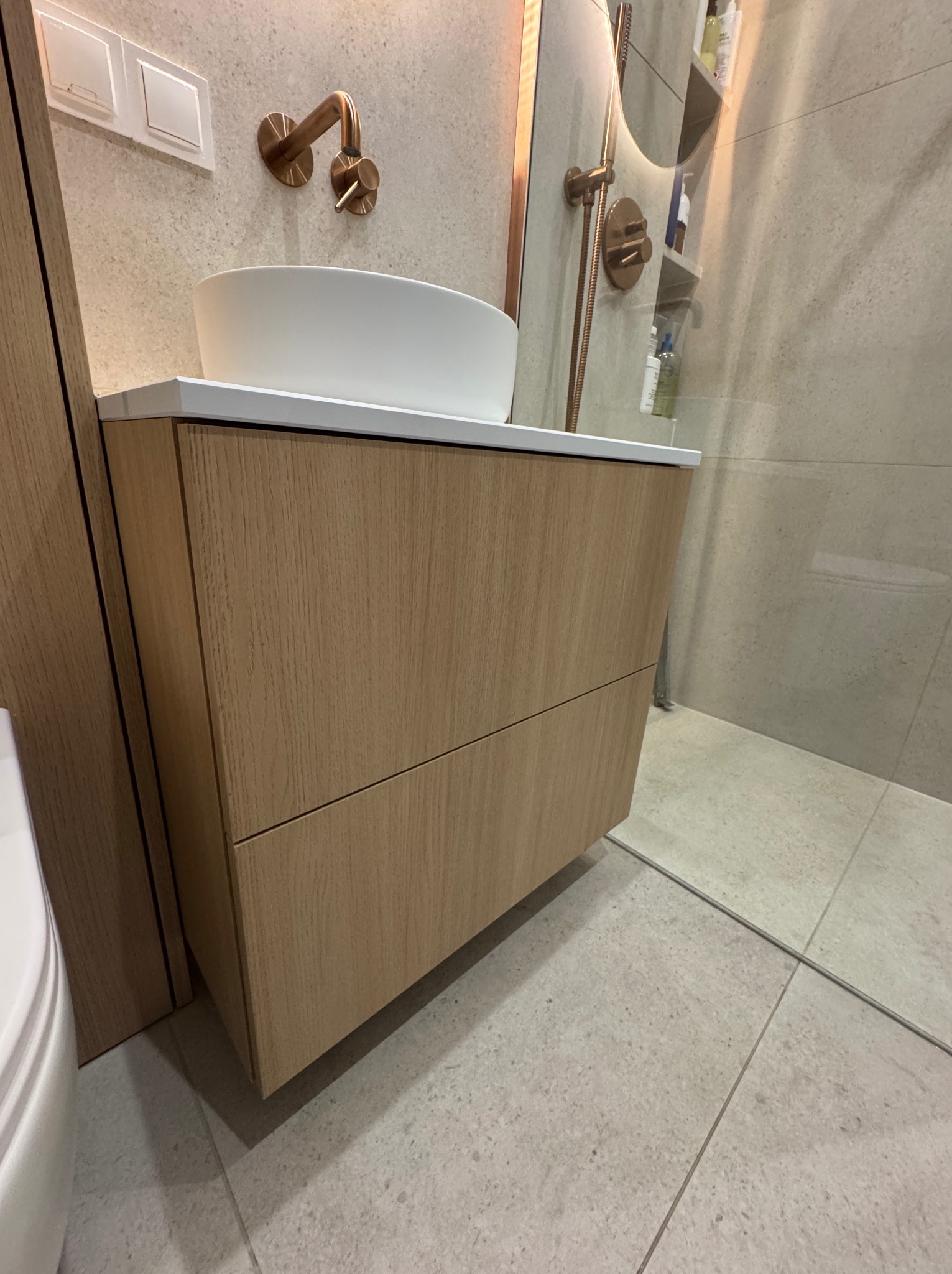 Nowoczesna szafka łazienkowa z umywalką nablatową i miedzianą armaturą. Minimalistyczny design, ciepłe oświetlenie, jasne płytki. Ujęcie z bliska.