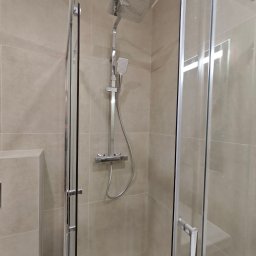 BUD-RAF Ślebocki Rafał - Nowoczesna kabina prysznicowa z deszczownicą i szklanymi drzwiami przesuwnymi, wykończona beżowymi płytkami. Minimalistyczny design, chromowane elementy.