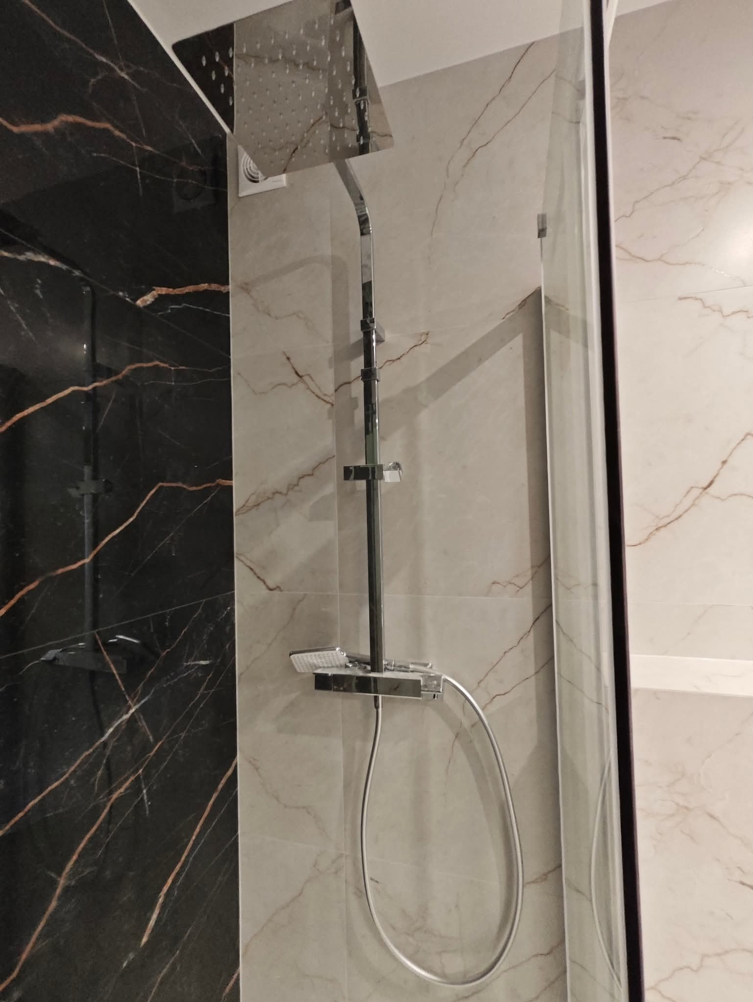 Nowoczesna kabina prysznicowa z deszczownicą i marmurowymi płytkami w odcieniach bieli i czerni z złotymi żyłami, widok z bliska na armaturę.