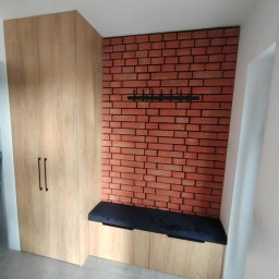 Bartek Wojtasik - Funkcjonalna szafa z siedziskiem i wieszakiem na tle ściany z cegły w przedpokoju. Jasne drewno, czarne detale, nowoczesny design.