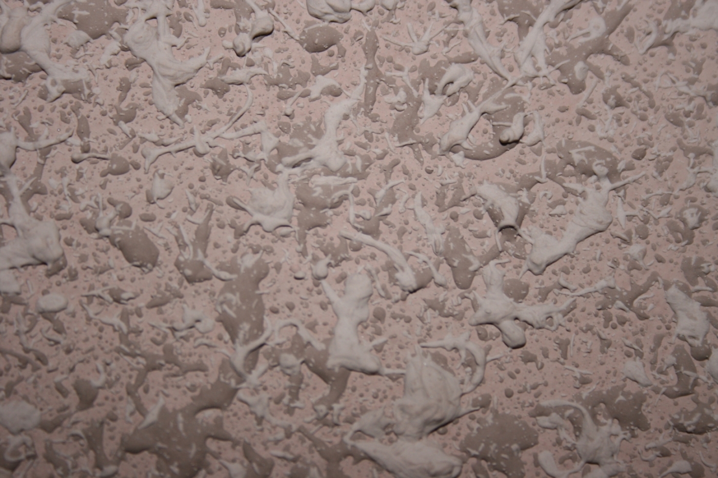 Szczegółowe zbliżenie ściany pokrytej tapetą natryskową w odcieniach beżu i bieli, tworzącą nierównomierną, teksturowaną powierzchnię.