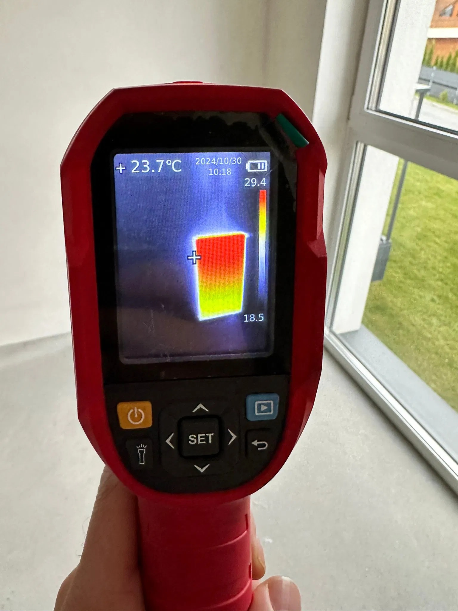 Termowizja okna: czerwony termometr pokazuje rozkład temperatur na szybie, z datą 2024/10/30. Widoczne okno z zielonym trawnikiem w tle.