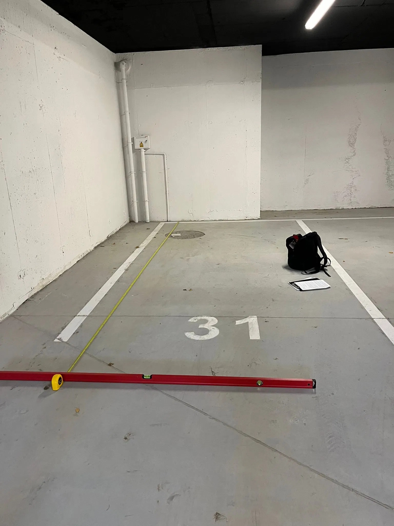 Oznakowane miejsce parkingowe nr 31, z poziomnicą, miarką i torbą. Kontrola wymiarów i zgodności z projektem. Szare ściany i podłoga, białe linie.